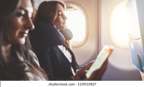 Two Females Going On Business Trip By Plane. A Woman Reading An E-book On A Smartphone