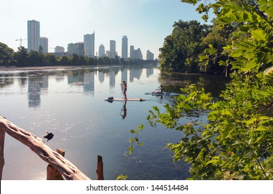 Two Females Paddle Boarding On Ladybird Lake With Downtown Austin, TX In The Background.