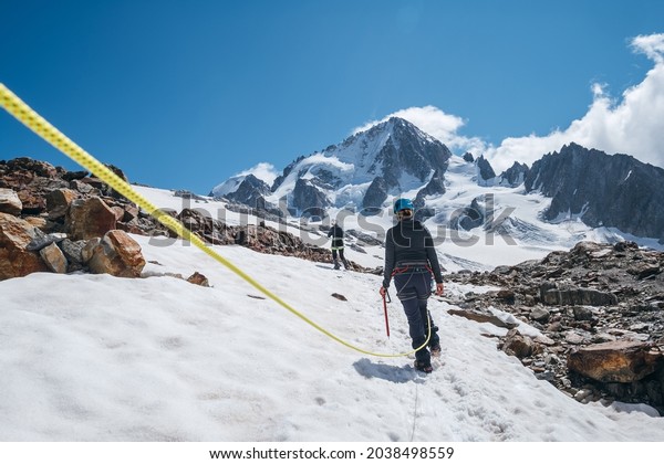 Two females Rope team members on
acclimatization day dressed in mountaineering clothes walking in
crampons with ice axes by snowy slopes in a climbing harness and
dynamic rope on close-up
foreground