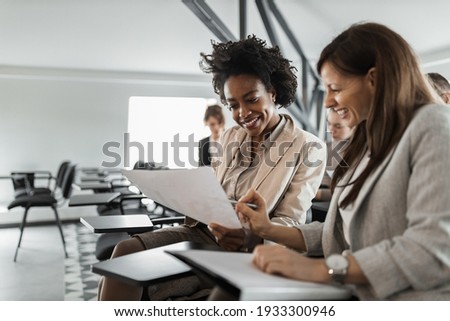 Two females in a suits, doing paper work.