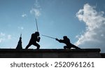 Two fencers dressed in black protective uniforms, helmets with face masks are fencing on castle wall using long medieval metal historical swords practicing before competition s. Active people concept