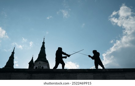 Two fencers dressed in black protective uniforms, helmets with face masks are fencing on castle wall using long medieval metal historical swords practicing before competition s. Active people concept - Powered by Shutterstock