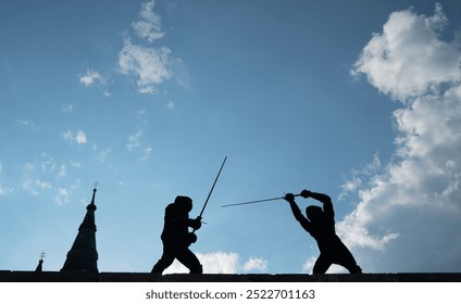 Two fencers dressed in black protective uniforms, helmets with face masks are fencing on castle wall using long medieval metal historical swords practicing before competition s. Active people concept - Powered by Shutterstock