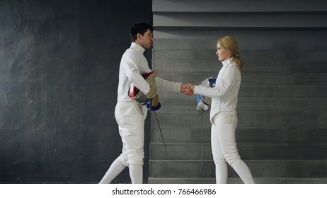 Two fencers man and woman shake hands each other at the end of fencing competition indoors - Powered by Shutterstock