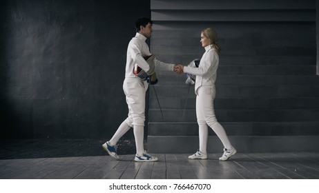 Two fencers man and woman shake hands each other at the end of fencing competition indoors - Powered by Shutterstock