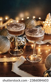 Two festive chocolate mousses in cocktail glasses. A layer of dark chocolate coffee mousse and a layer of light cream mousse with grated chocolate on top. Christmas lights and decorations. 