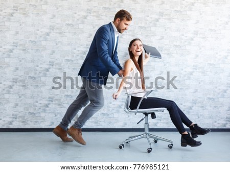 Two ffice workers having fun at work, a guy rolling a girl on an chair on wheels.