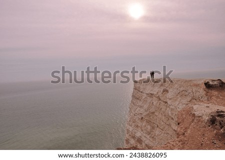 Two figures standing on the edge of chalk cliffs looking at the setting sun