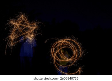 Two figures use sparklers to create a glowing star and a swirling circle against a dark background.
