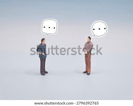 Two figurines with speech bubbles pause in dialogue, representing communication, hesitation, silence, contemplation, and interpersonal connection in abstract human exchange.