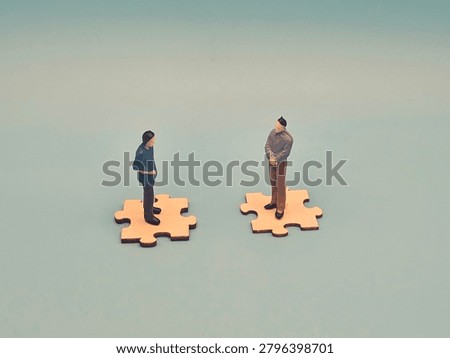 Two figurines stand on separate puzzle pieces that complement each other, symbolizing connection, interdependence, teamwork, and the idea of unity through fitting parts.