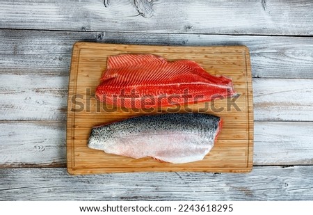Two fillet, skin side up and down, of trout salmon on cutting board with white rustic wooden table background  