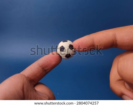 Two fingers balance a tiny black and white miniature toy soccer ball against a clear blue background.