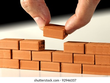 Two fingers put the last brick on the wall. Metaphoric scene