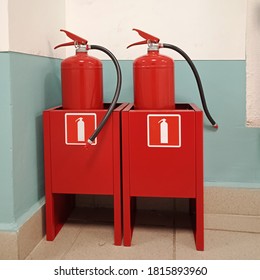 Two fire extinguishers in containers are in the corner for fire safety.