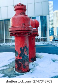 Two fire hydrants are located on a snowy sidewalk next to a modern building. The city is bustling with activity as winter weather is present.