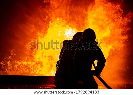 Two firefighter holding fire fighting nozzles for extinguish fire.Teamwork shoot water for reduce dangerous from conflagration fire.Train emergency team.