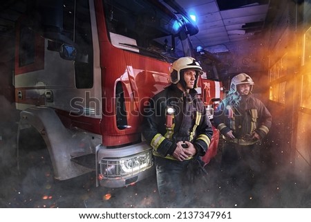 Two firefighters dressed in workwear with helmets in fire station