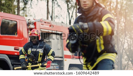 Two firefighters in fire fighting operation, fireman in protective clothing and helmet with equipment in action fighting