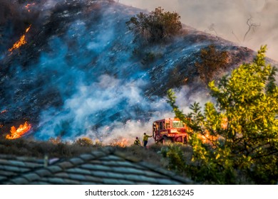 Two Firefighters Lean On Bulldozer With Burning Hillside In Back