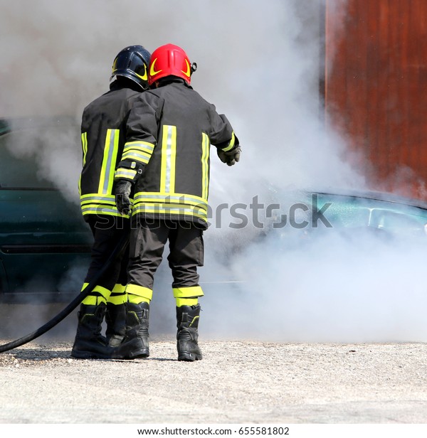 Two\
firefighters with uniform and protective helmet extinguish the fire\
of the incident car during a firefighting\
exercise