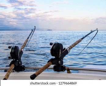 Two fishing rods held in fishing rod holders, attached to a back of a boat.  The rods are bent from the weight of the down riggers.  People are trolling for salmon of the coast of British Columbia.