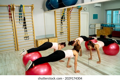 Two Fit Girls In A Gym, Doing Plank Exercise On Swiss Ball 