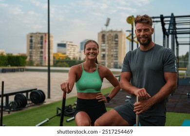 Two fit individuals, a man and a woman, posing with sledgehammers on a large tire in an outdoor gym setting. They are dressed in athletic wear and appear ready for a workout. - Powered by Shutterstock