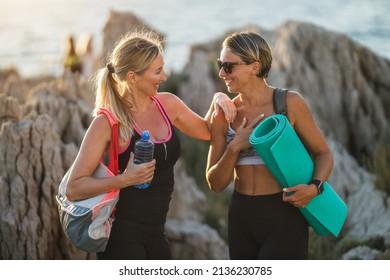 Two fit smiling middle age women are talking and holding a sports mat before doing yoga exercises during training near the sea beach. - Powered by Shutterstock