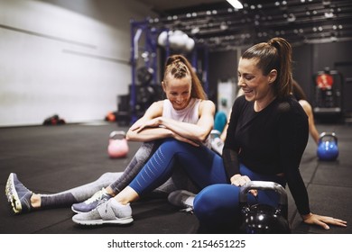 Two Fit Women In Sportswear Laughing While Sitting Together On The Floor Of A Gym After An Exercise Class