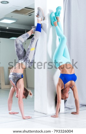 Two fit young Caucasian girls wearing sportswear performing handstand against wall indoors