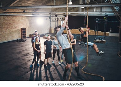 Two fit young men climbing ropes in a gym with people on the floor watching - Powered by Shutterstock