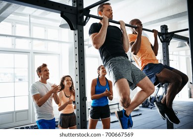 Two fit young men having a pullups competition in a gym with a diverse group of friends cheering them on in the background - Powered by Shutterstock