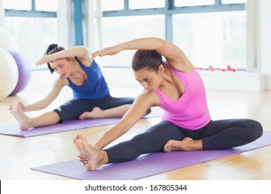 Two fit young women doing stretching pilate exercises in fitness studio - Powered by Shutterstock
