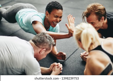 Two Fit Young Women In Sportswear Laughing And High Fiving Together While Planking With A Couple Of Friends During A Gym Class