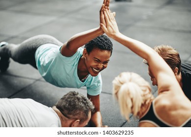 Two Fit Young Women In Sportswear Laughing And High Fiving While Planking With A Couple Of Male Friends On The Floor Of A Gym