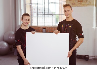 Two fitness instructors at a ems gym, a young man and woman holding a blank white sign with copy space and smiling at the camera - Powered by Shutterstock