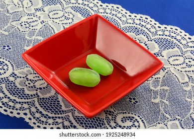 Two Fizzy Lime Hard Candy Pieces In Red Candy Dish On Lace Table Runner On Blue Tablecloth