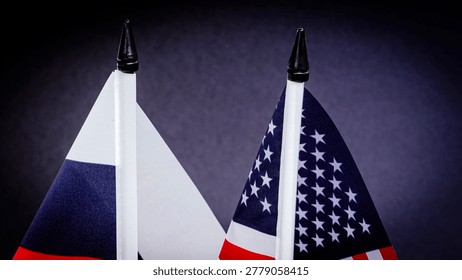 Two flags stand close, representing opposing nations. Dark background highlights their colors and shapes. Tops are pointed, showing careful arrangement