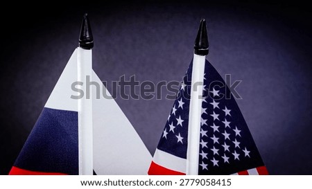 Two flags stand close, representing opposing nations. Dark background highlights their colors and shapes. Tops are pointed, showing careful arrangement