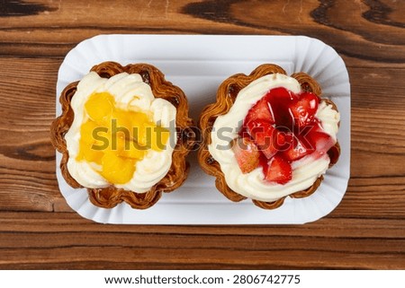 Two flaky layered fruit tarts filled with creamy custard, one topped with fresh mango cubes and the other glazed strawberry chunks
