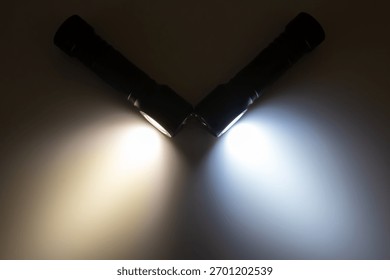 Two flashlights are positioned at an angle, casting beams of warm and cool light. Their illumination highlights the surrounding darkness, perfect for exploring unknown areas at night.