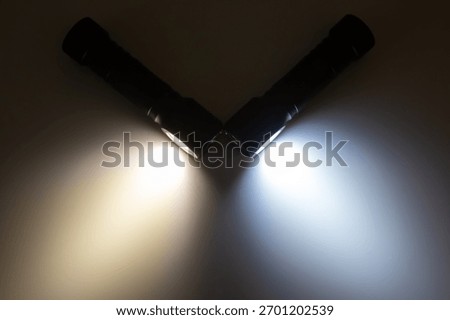 Two flashlights are positioned at an angle, casting beams of warm and cool light. Their illumination highlights the surrounding darkness, perfect for exploring unknown areas at night.
