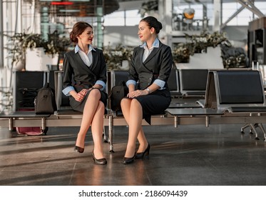 Two Flight Attendants Sitting On The Seats And Talking In The Airport Terminal