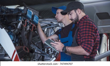 Two Flight Mechanics Doing A Pre Flight Check Or Maintenance On A Small Single Engine Aircraft Using Digital Tablet In A Hangar In A Close Up View Of Them Working On The Engine.