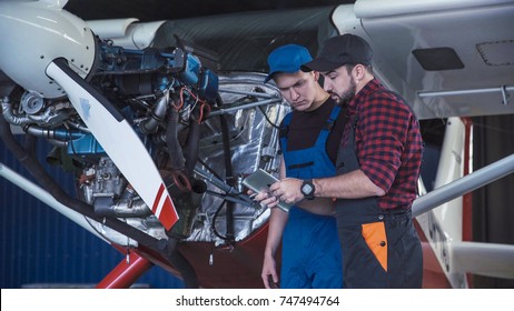 Two Flight Mechanics Doing A Pre Flight Check Or Maintenance On A Small Single Engine Aircraft In A Hangar In A Close Up View Of Them Working On The Engine.