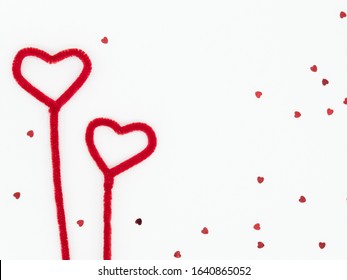 Two fluffy red hearts made from pipe cleaners with scattered heart glitter on white background