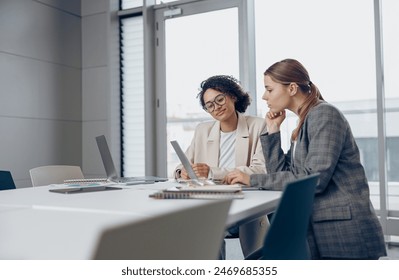 Two focused female coworkers working on project together and use laptop sitting in office - Powered by Shutterstock