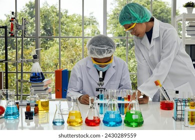 Two focused laboratory scientists conducting a detailed chemical analysis, with one using a microscope and the other handling a petri dish - Powered by Shutterstock