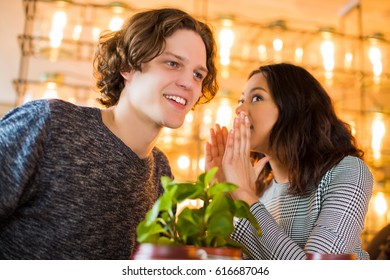Two focused students sit in cafe and  a woman speaks something to a man`s ear, inside